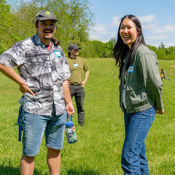 Three people casually standing and smiling in a sunny, open grassy field with trees in the background.